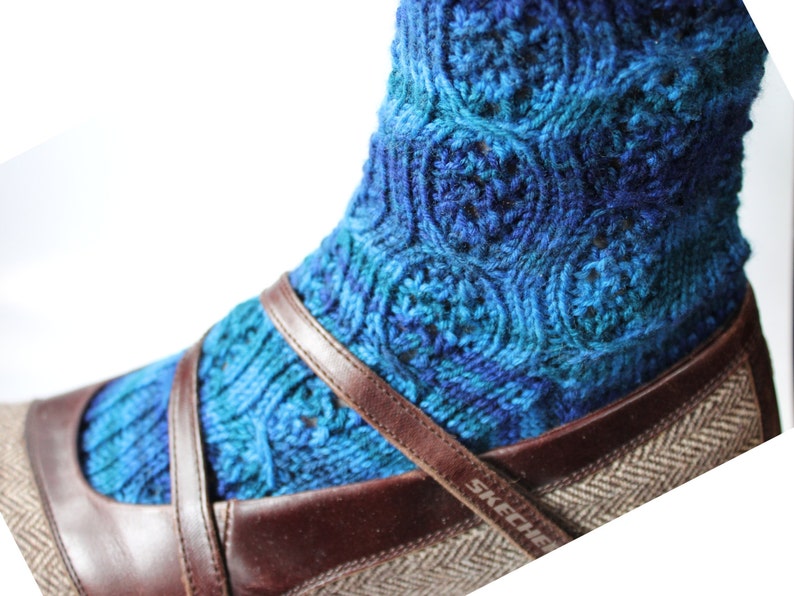 May include: Blue and teal knitted socks with a swirling pattern, worn with brown leather shoes with a brown and white herringbone pattern. The shoes have the word "SKECHERS" on the side.
