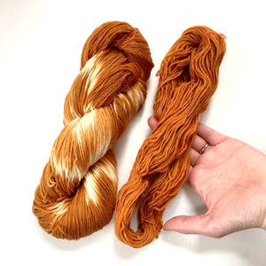 May include: Two skeins of yarn, one is a solid orange color and the other is a variegated orange and white color.