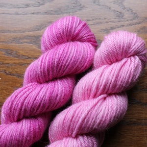 Op de afbeelding: Twee bollen roze garen, een in een donkerdere roze tint en de andere in een lichtere roze tint.