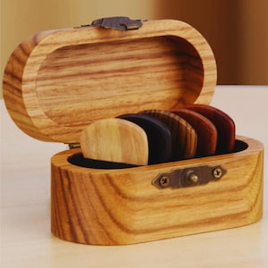 May include: A wooden box with a hinged lid and a brass clasp. The box contains a set of six guitar picks made from different types of wood.