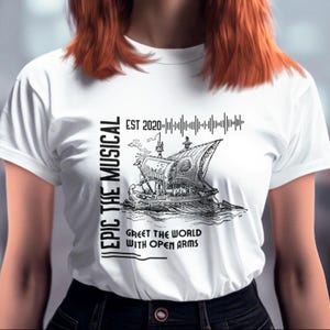 May include: White t-shirt with a black graphic of a ship on the sea, with the text "EPIC THE MUSICAL" on the left side and "EST 2020" above the ship. The text "GREET THE WORLD WITH OPEN ARMS" is below the ship.