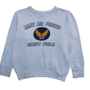 May include: A light blue sweatshirt with a navy blue and yellow graphic of a winged star with the text "Army Air Forces Scott Field" around it.