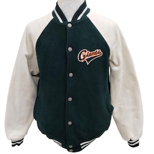 May include: A green and white varsity jacket with a white and black striped collar and cuffs. The jacket has a large "Giants" logo on the front in orange and black lettering.
