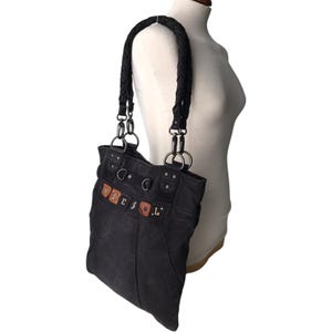 May include: Black tote bag with a braided handle and silver-tone hardware. The bag features the word "DIESEL" in brown and tan letters. The bag is made of a dark, textured material.