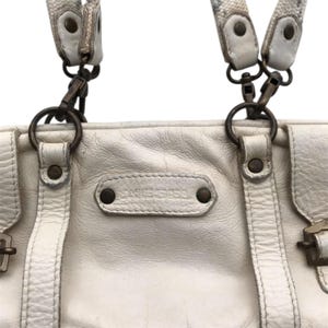 K&ouml;nnte beinhalten: Cremefarbene Lederhandtasche mit dem Markennamen "DIESEL" auf der Vorderseite. Die Tasche hat zwei obere Griffe mit gemusterten Riemen und Metallbeschl&auml;gen. Die Tasche hat eine rechteckige Form und ein leicht abgenutztes Aussehen.