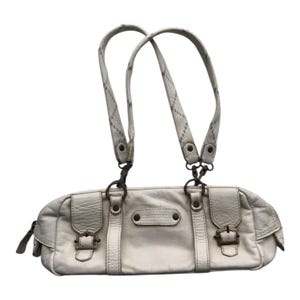 K&ouml;nnte beinhalten: Cremefarbene Lederhandtasche mit zwei Tragegriffen und einer langen, rechteckigen Form. Die Tasche hat zwei Vordertaschen mit Schnallenverschl&uuml;ssen und einen Rei&szlig;verschluss. Die Griffe sind hellgrau mit einem dezenten Muster.