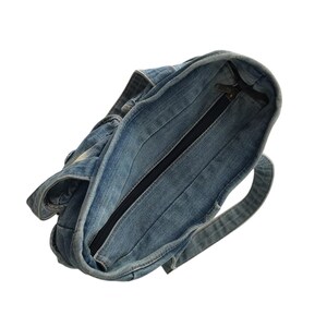 May include: A denim tote bag with a zipper closure. The bag is made of light blue denim fabric and features a black zipper. The bag has a handle and is designed for carrying items.
