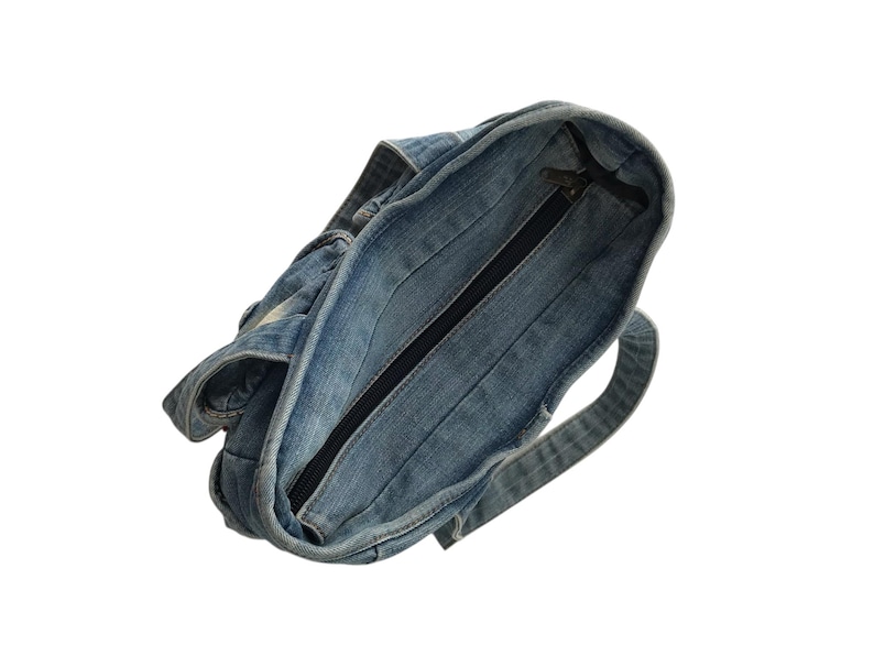 May include: A denim tote bag with a zipper closure. The bag is made of light blue denim fabric and features a black zipper. The bag has a handle and is designed for carrying items.