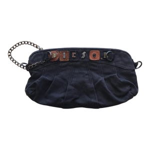 May include: A black canvas clutch bag featuring a dark metal chain strap. The top panel is adorned with a series of brown leather squares, each displaying individual metal letters that spell out DIESEL, along with decorative metal hardware.