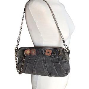 May include: A charcoal gray denim handbag featuring a pleated front, a detachable silver-tone metal chain strap, and a top zipper closure. The front is decorated with a row of mixed leather and metal square patches spelling out the word DIESEL.