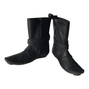 May include: A pair of black leather boots with a mid-calf height. The boots feature a side zipper and a wrap-around strap design. The soles are stitched, and the boots have a pointed toe.