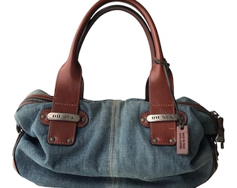May include: A blue denim handbag with brown leather handles and accents. The bag features a zipper closure and metal Diesel tags. A small tag reads "MADE IN ITALY 100% LEATHER."
