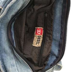 May include: A denim handbag with a black zipper and a black interior. The bag features a Diesel Spare Parts label. The denim is a light blue wash.