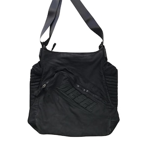 May include: Black messenger bag with a shoulder strap. The bag features a large front pocket with the embossed word "DIESEL". The bag has a zippered closure and a textured design on the sides.