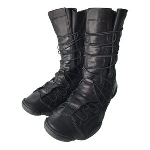Könnte beinhalten: Ein Paar schwarze Lederstiefel mit mittelhohem Schaft. Die Stiefel haben ein Schnürdesign mit schwarzen Schnürsenkeln und eine runde Spitze. Das Leder hat ein leicht abgenutztes Aussehen.