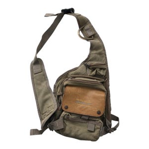 Può includere: Borsa a tracolla in tela verde oliva con più tasche e una toppa in pelle marrone. La borsa è dotata di una lunga tracolla regolabile e di una chiusura con fibbia. Il testo "DIESEL" è visibile sulla toppa in pelle.