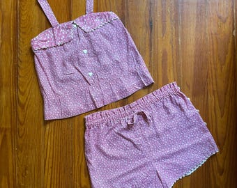 Op de afbeelding: Een tweedelige pyjamaset met een roze bloemenprint. De top heeft een geschulpte kraag en bandjes, met hartvormige knopen. De shorts hebben een taille met trekkoord en een geschulpte zoom. De set is gemaakt van een lichte stof.