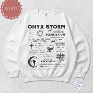 May include: White sweatshirt with the text "ONYX STORM" and various graphics, including a sun, bats, and a crescent moon. The design includes phrases like "The Sky Belongs To Us" and "We Are The Reckoning."