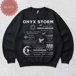 May include: Black Onyx Storm sweatshirt with white text and graphics. The design includes phrases like "Equilibrium," "The Sky Belongs to Us," and "We Are the Reckoning." A celestial theme with moons, stars, and lightning bolts.