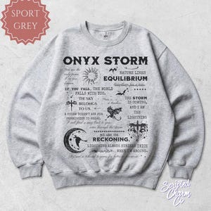 May include: Sport grey sweatshirt with the text "ONYX STORM" and various graphics. The design includes phrases like "Nature likes equilibrium" and "We are the reckoning." The sweatshirt has a crew neck and long sleeves.