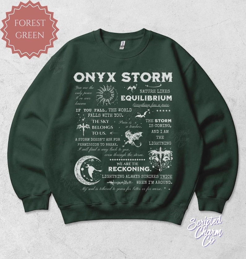 May include: Forest green sweatshirt with the text "ONYX STORM" and various quotes and illustrations. The design includes a sun, moon, stars, and other celestial elements. The sweatshirt is a crew neck style.