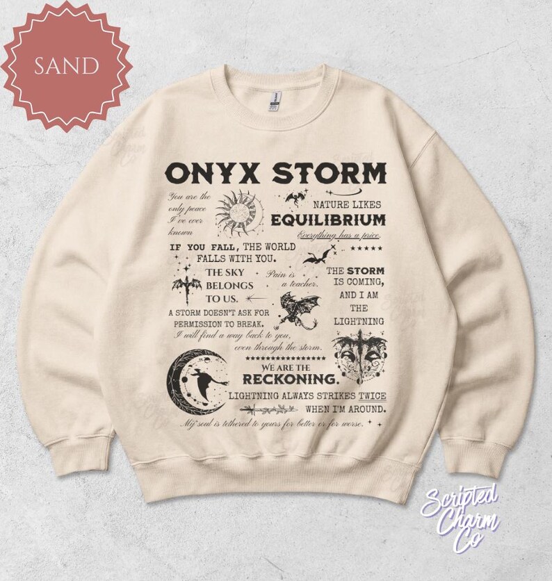 May include: Sand-colored sweatshirt with the text "ONYX STORM" and various graphics, including a sun, stars, and a bat. The design features several lines of text with inspirational quotes. The sweatshirt is a crew neck.