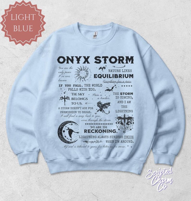 May include: Light blue Onyx Storm sweatshirt with black text and graphics. The design includes phrases like "The Sky Belongs to Us" and "We Are The Reckoning." Features a crew neck and long sleeves. The sweatshirt is a comfortable, casual wear item.