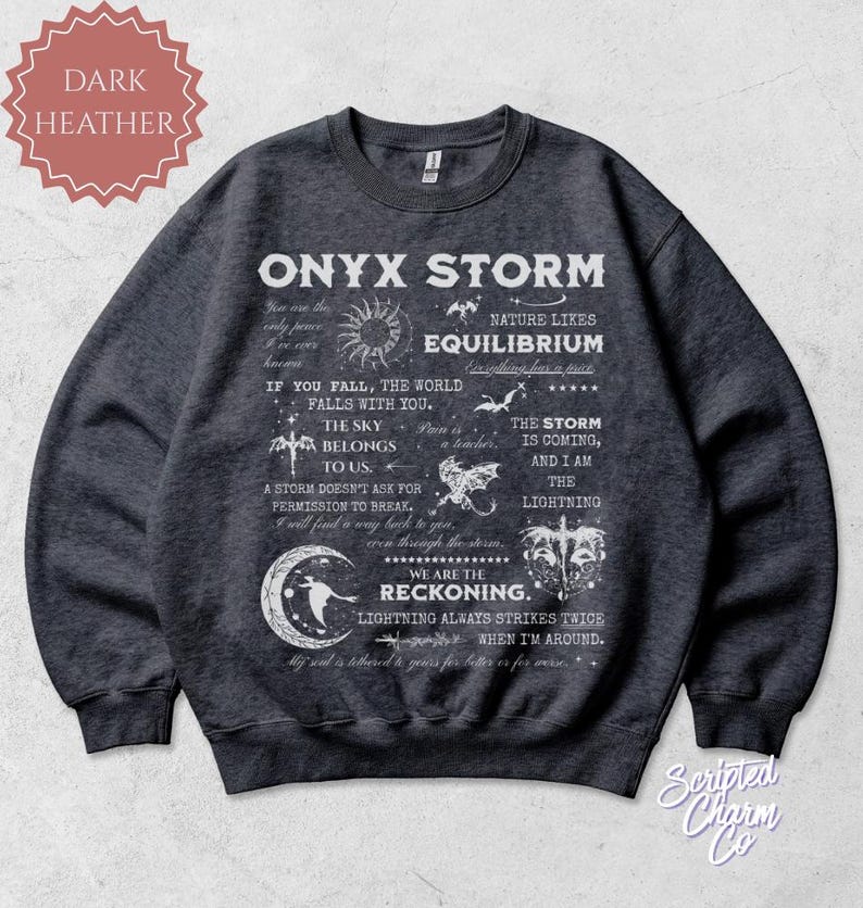 May include: Dark heather gray sweatshirt with the text "ONYX STORM" and other phrases and graphics in white. The sweatshirt has a crew neck and long sleeves. The brand name "Scripted Charm Co" is in the bottom right corner.