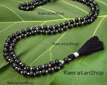 May include: A dark brown beaded necklace with a black tassel. The beads are strung on a silver-colored string. The necklace is displayed on a large green leaf. The text "RamratanShop" is visible.