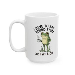 May include: White ceramic mug featuring a cartoon frog holding a coffee cup. The frog is green with a yellow belly and is standing on grass. Text on the mug reads "I HAVE TO SAY WEIRD STUFF OR I WILL DIE."