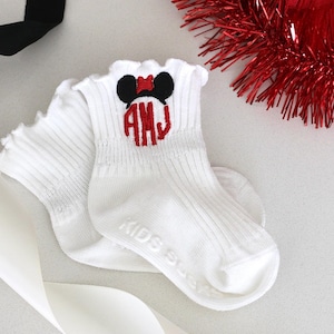 May include: A pair of white ankle socks with a red and black embroidered Mickey Mouse head and the monogram "AHJ".