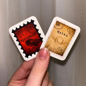 May include: Two vintage-style postage stamps, one red with a black raven and the text "15c KETTERDAM", the other beige with a crescent moon and the text "15c RAVKA".