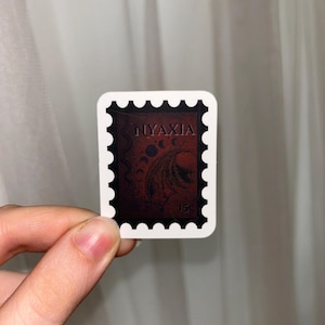 May include: A white sticker with a black border and a red stamp inside. The stamp has a black and white image of a dragon with the word "NYAXIA" printed in white.