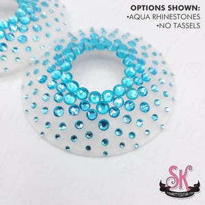 May include: Two circular white mesh fabric pieces embellished with aqua rhinestones of varying sizes. The text OPTIONS SHOWN: AQUA RHINESTONES NO TASSELS is printed in the upper right corner. A logo with the letters SK is in the bottom right.