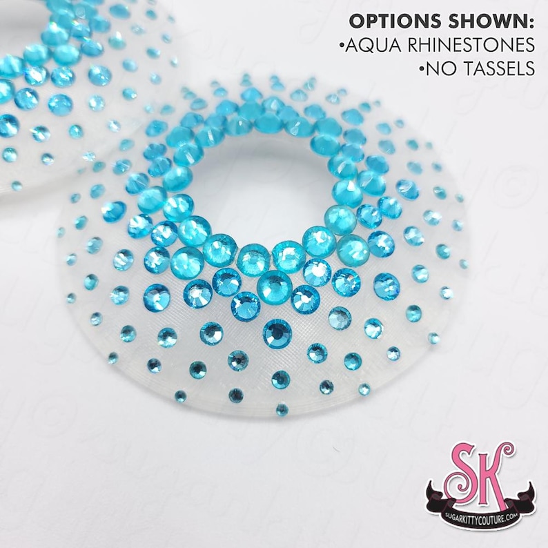 May include: Two circular white mesh fabric pieces embellished with aqua rhinestones of varying sizes. The text OPTIONS SHOWN: AQUA RHINESTONES NO TASSELS is printed in the upper right corner. A logo with the letters SK is in the bottom right.