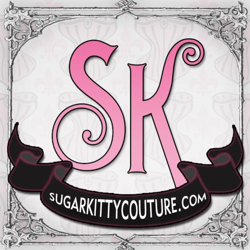 May include: A square logo featuring large, stylized pink letters S and K centered above a black ribbon banner. The banner contains the white text SUGARKITTYCOUTURE.COM. The entire design is enclosed within a decorative, ornate gray border.