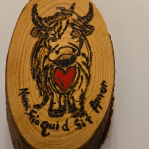 May include: A wooden disc with a black and white drawing of a cow holding a red heart. The text "Nuncio quid Sit Amor" is written around the cow.