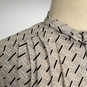 Puede incluir: Una camisa blanca y negra con un patrón geométrico de cuello alto. El patrón presenta líneas negras y pequeños puntos blancos sobre un fondo blanco.