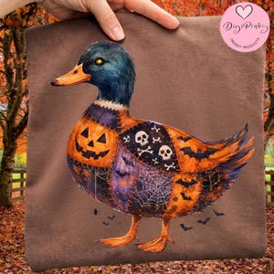 May include: A brown t-shirt featuring a graphic of a duck with a patchwork design. The duck has a jack-o'-lantern chest, a wing with skulls and crossbones, and a section with spiderwebs and bats. The duck has a blue head and orange beak.