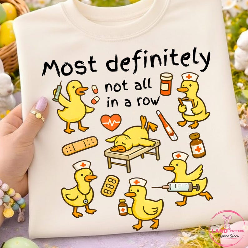 Pu&ograve; includere: Felpa color crema con una grafica raffigurante anatre gialle dei cartoni animati in ruoli medici, con la scritta "Most definitely not all in a row". Le anatre sono raffigurate con siringhe, pillole e bende.