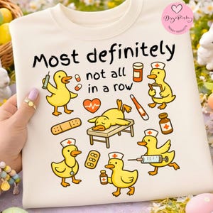 Puede incluir: Sudadera color crema con un gráfico lúdico que presenta patos de dibujos animados amarillos en roles médicos, rodeados de suministros médicos. El texto "Most definitely not all in a row" se muestra encima de los patos. Un logotipo de Digi Pinky Trendy Products.