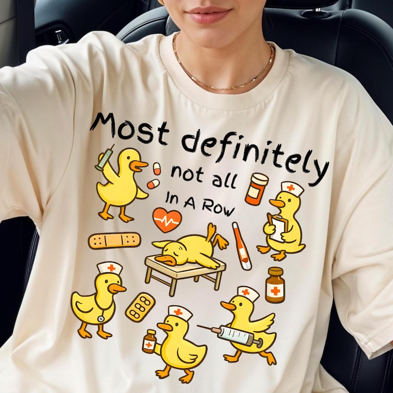 Pu&ograve; includere: T-shirt color crema con la scritta "Most definitely not all In A Row" e anatre dei cartoni animati con cappelli da infermiera. Le anatre tengono in mano forniture mediche come siringhe, pillole e bende. La maglietta ha uno scollo tondo.