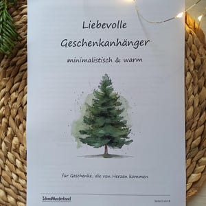 May include: A white paper with the text "Liebevolle Geschenkanhänger" and a watercolor illustration of a green Christmas tree. The paper is on a woven, light brown surface. The text "minimalistisch & warm" is also visible.