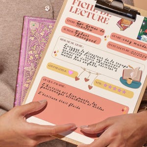 Puede incluir: Un portapapeles de madera con un registro de lectura en franc&eacute;s, titulado "FICHE DE LECTURE", que detalla el t&iacute;tulo del libro "Les dames de Marlow", el autor Robert Thorogood y el g&eacute;nero "cosy murder". Un libro y un libro morado se sostienen juntos.