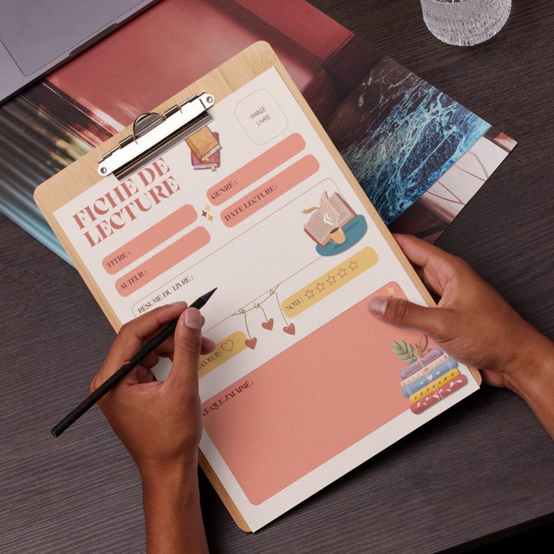Puede incluir: Un portapapeles de madera con un registro de lectura impreso titulado "FICHE DE LECTURE". El registro incluye secciones para el t&iacute;tulo, el autor, el g&eacute;nero y las notas, decorado con ilustraciones de libros y una guirnalda de corazones. Una mano sostiene un bol&iacute;grafo sobre el registro.