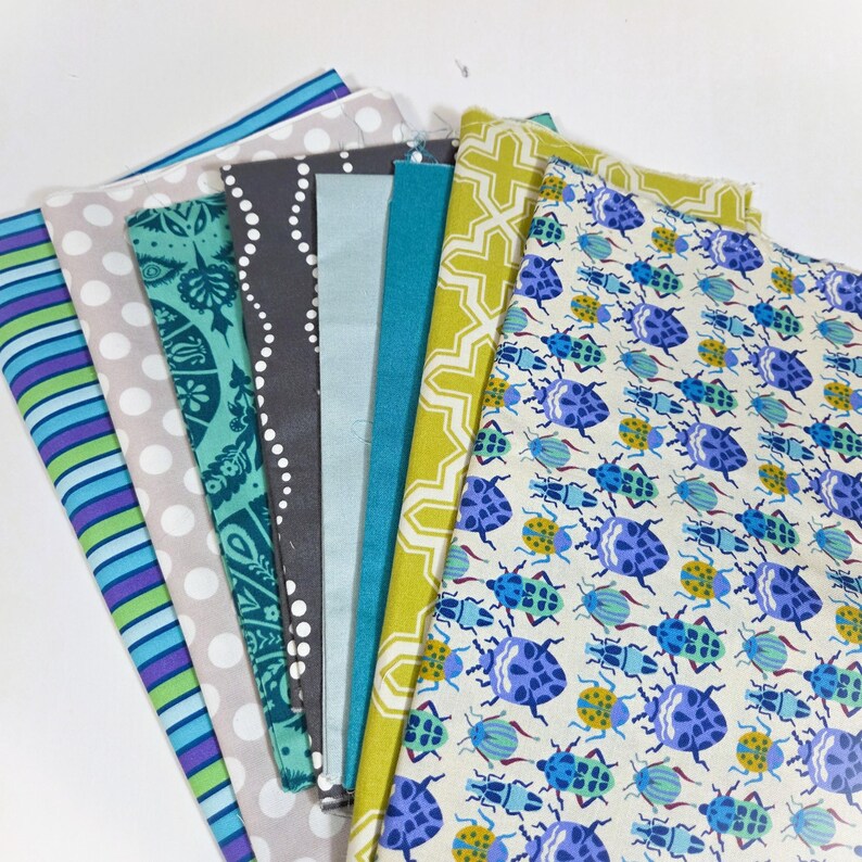 May include: A collection of colorful fabric swatches. Patterns include stripes, polka dots, floral designs, and geometric shapes. Colors include blue, green, gray, and yellow. One fabric features a repeating pattern of blue and yellow beetles.