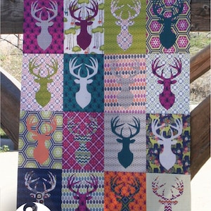 May include: A quilt with a patchwork design featuring a repeating pattern of deer silhouettes in various colors and patterns. The quilt is titled "BIG GAME" and is signed "EMILY HERRICK".