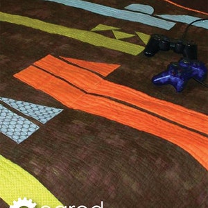 Peut inclure: Fond marron avec le mot « GAMER » en blanc. L'image présente des formes abstraites orange, bleues et vertes, ainsi que deux manettes de jeu. Le texte « Geared for Guys » et « Crazy Old Ladies » sont également présents.