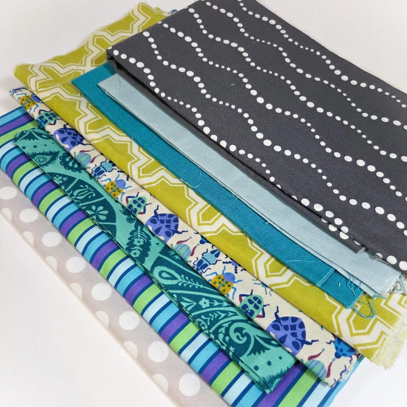 May include: A collection of fabric swatches in various colors and patterns. Designs include white polka dots, wavy white lines on gray, geometric shapes, and insect motifs. Colors include teal, green, blue, and gray.