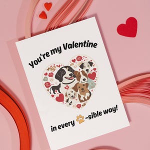 Pode incluir: Um cartão branco com o texto "You're my Valentine in every paw-sible way!" e uma ilustração em forma de coração de cães. O coração está cheio de pequenos corações, flores e pegadas.